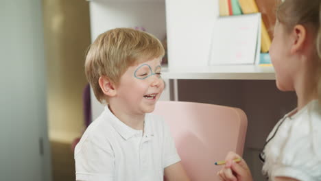Girl-paints-glasses-on-younger-boy-face-and-children-smile