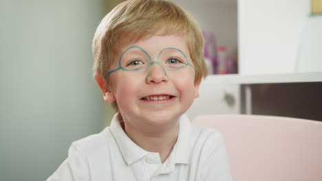 Cute-toddler-with-painted-glasses-smiles-looking-at-camera