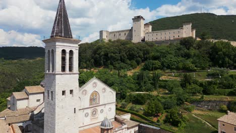 Aerial-Flying-Past-Spoleto-Cathedral-Bell-Tower-With-Rocca-Albornoziana-In-Background-On-Hill-Top