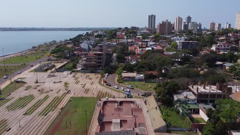 Drone-fly-over-skatepark-and-surrounding-city-and-ocean,-pan-down-to-BMXing-kids