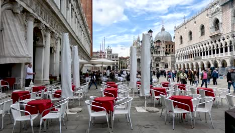 Sillas-De-Café-Vacías-Con-Turistas-Pasando-Por-La-Plaza-De-San-Marcos-En-Venecia