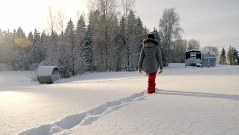 Shot-of-a-woman-in-black-warm-winter-coat-and-red-pant,-walking-through-thick-layer-of-white-snow-towards-her-vacation-cabin-before-looking-back-on-her-path