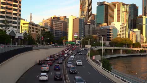 Dynamische-Zoom-Out-Aufnahme,-Die-Den-Ein--Und-Ausgehenden-Fahrzeugverkehr-Zur-Hauptverkehrszeit-Auf-Der-Pazifikautobahn-M3-Mit-Der-Innenstadtlandschaft-Am-Flussufer-Im-Hintergrund-Bei-Goldenen-Stunden-Des-Sonnenuntergangs-Einfängt