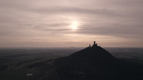 Silhouette-Einer-Mittelalterlichen-Burg-Auf-Einem-Hügel-Mit-Sonnenuntergang-Am-Horizont,-Drohnenaufnahme