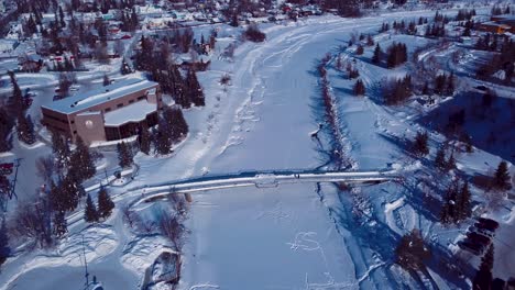 Video-De-Drones-De-4k-De-Peatones-Caminando-Por-Un-Puente-Sobre-El-Río-Chena-Congelado-En-El-Centro-De-Fairbanks,-Alaska,-En-Un-Día-Nevado-De-Invierno