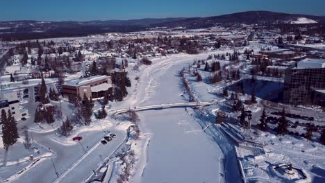 4K-Drohnenvideo-Von-Menschen,-Die-An-Einem-Verschneiten-Wintertag-über-Die-Fußgängerbrücke-über-Den-Zugefrorenen-Chena-River-In-Der-Innenstadt-Von-Fairbanks,-Alaska,-Gehen