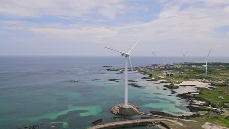 Stunning-drone-view-of-Woljeong-Beach's-pristine-shores,-a-tranquil-oasis-on-beautiful-Jeju-Island,-with-a-unique-view-of-Wind-Turbines-in-right-on-the-waters-edge