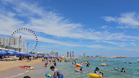Menschen-Schwimmen-Am-Strand-Von-Sokcho-Mit-Riesenrad-In-Der-Ferne-Im-Sommer-In-Sokcho,-Südkorea