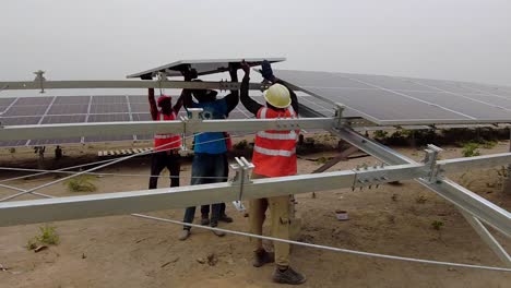Cámara-Lenta-De-Un-Técnico-Que-Trabaja-En-Equipo-Instalando-Paneles-Solares-En-Una-Estación-Base-Fotovoltaica-En-África-Para-El-Desarrollo-Del-Suministro-De-Energía-Renovable---Jambur,-Gambia