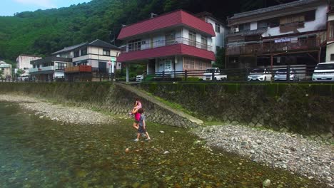 La-Vista-Del-Dron-Captura-Un-Momento-Sereno-En-La-Aldea-De-Koyasan,-Japón,-Mientras-Una-Madre-Con-Dos-Hijos-Atraviesa-El-Río-A-Pie,-Conectados-Por-Su-Tranquilo-Abrazo.