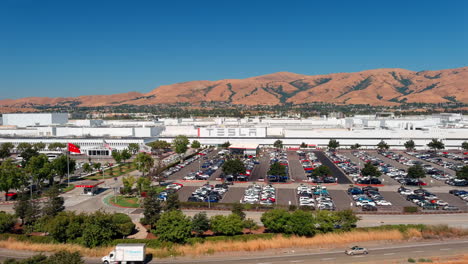 Vista-Aérea-Acercándose-A-La-Enorme-Sala-De-Exposición-De-Automóviles-Eléctricos-Tesla-En-Fremont,-California,-Bajo-Un-Paisaje-De-Montaña