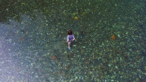 Der-Hohe-Winkel-Der-Drohne-Fängt-Einen-Jungen-Männlichen-Entdecker-In-Einem-Klaren-Fluss-Ein-Und-Gibt-Den-Blick-Auf-Das-Atemberaubende-Flussbett-Frei