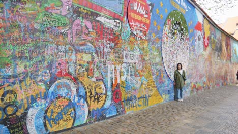 Frau-Steht-Vor-Der-John-Lennon-Mauer-In-Prag,-Tschechische-Republik-–-Inspirierte-Graffiti,-Texte-Aus-Beatles-Liedern-Und-Designs-Im-Zusammenhang-Mit-Lokalen-Und-Globalen-Anliegen