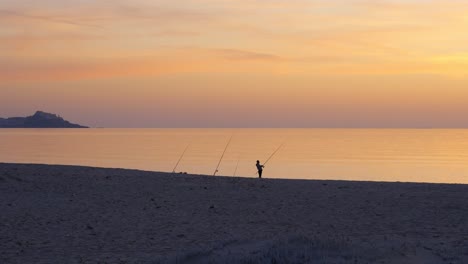 Silhouette-Einer-Person,-Die-Bei-Sonnenuntergang-Am-Meeresufer-Fischt