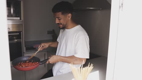 Content-ethnic-man-frying-tomatoes-on-pan-in-kitchen