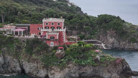 Beautiful-red-hotel-Mezzatorre-on-a-rocky-cliff-at-the-Ischia-coast-in-Italy