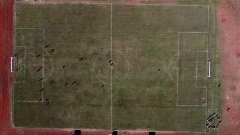 Drone-look-down-and-strafe-over-football-pitch-with-football-match-being-played---players-defend-goal