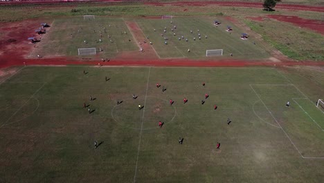 Drone-fly-over-football-matches-being-played-on-three-football-fields,-one-in-foreground-and-two-in-the-background