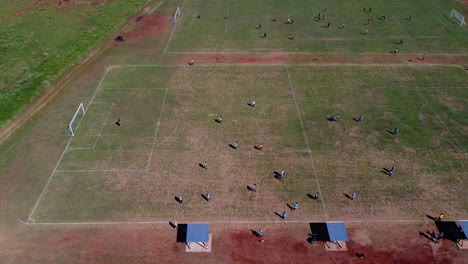 Drone-high-altitude-strafe-past-kids-playing-football,-multiple-football-pitches-at-Posadas-hipodrome