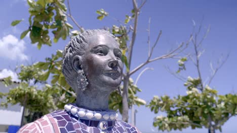 Inmitten-Des-üppigen-Grüns-Ziert-Eine-Statue-Einer-Schönen-Frau-Die-Szene-In-Barranquilla,-Während-Sanft-Verschwommene-Bäume-Eine-Ruhige-Kulisse-Schaffen