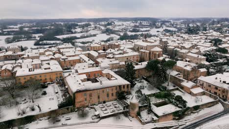 Aerial-view-of-Monpazier-church-in-the-snowy-morning,-streets-empty,-market-square-visible,-Dordogne,-France