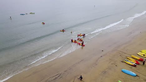 Bird's-eye-view-of-kayakers-pushing-off-from-beach-in-La-jolla-california,-calm-day