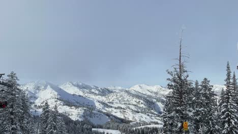 Handheld-landscape-shot-on-the-summit-of-a-ski-resort-in-the-Rocky-Mountains-in-Utah-with-the-lift-passing-by-and-surrounded-by-snow-covered-pine-trees-on-a-warm-winter-day