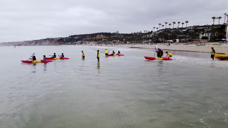 Aerial-dolly-to-kayakers-taking-off-from-cloudy-la-jolla-coastline