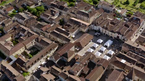 Drone-shot-of-the-place-de-Monpazier-during-a-cultural-event-that-takes-place-every-year,-white-stands-for-artisans-are-in-the-center-of-the-square,-Dordogne,-France