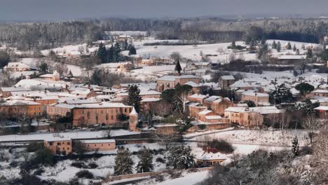 Monpazier-in-winter-under-the-snow-in-the-Dordogne,-circular-drone-shot-around-the-village,-the-streets-are-empty,-aerial-shot-in-the-morning