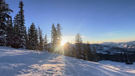 Wunderschöne-Winterlandschaft-Mit-Einem-Pfad-In-Einem-Skigebiet-In-Den-Rocky-Mountains-In-Utah-Mit-Vorbeifahrenden-Skifahrern-Während-Eines-Hellen,-Farbenfrohen-Sonnenuntergangs,-Der-An-Einem-Frühlingstag-Durch-Schneebedeckte-Kiefern-Führt