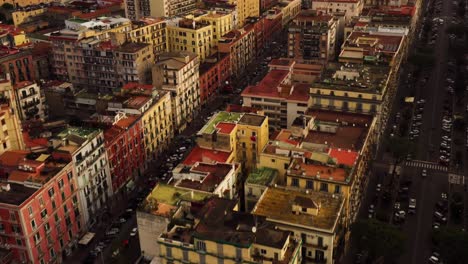 Aerial-birds-eye-flight-over-central-city-of-Naples-with-colorful-houses-and-roundabout-at-sunset---TIlt-up-shot-of-town-located-on-hill