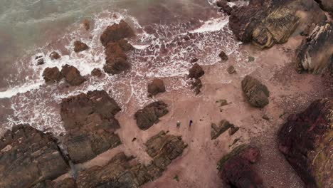 Drone-view-of-unrecognizable-traveler-standing-on-rocky-seashore