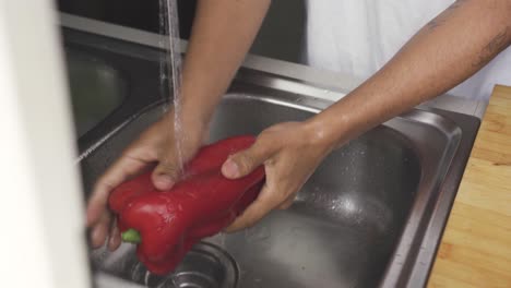 Anonymous-man-washing-bell-pepper-during-cooking-preparation