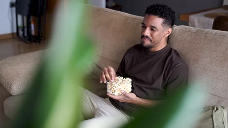Glücklicher-Ethnischer-Mann,-Der-Popcorn-Isst-Und-Auf-Dem-Sofa-Fernsieht