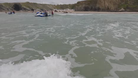 POV-shot-walking-back-to-shore-showing-tourists-getting-on-jet-skis-at-Lusty-Glaze,-Newquay