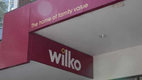 People-walk-past-a-Wilko-sign-that-reads,-“The-home-of-family-vale”-on-a-storefront-on-a-busy-high-street-in-Stratford-on-a-hot-summer-afternoon