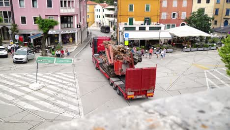 Articulated-lorry-pulling-trailer-with-tracked-excavator-through-village