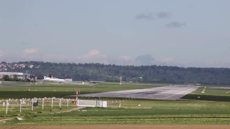 Flugzeug-Landet-Auf-Einem-Ländlichen-Flughafen-Mit-Wald-Und-Traktor-Fährt-Durch-Das-Feld
