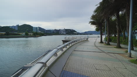 Walking-along-canal-river-railway-path-with-tiled-ground-in-Hong-Kong,-cloudy-day