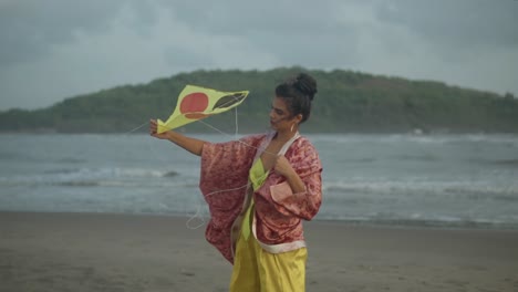Slow-motion-shot-of-a-young-woman-standing-at-a-sandy-beach-with-a-colorful-kite-in-her-hands