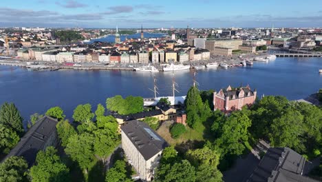 Drone-fly-over-Skeppholmen,-old-military-buildings-to-ship-in-the-river-and-Gamla-Stan-old-town