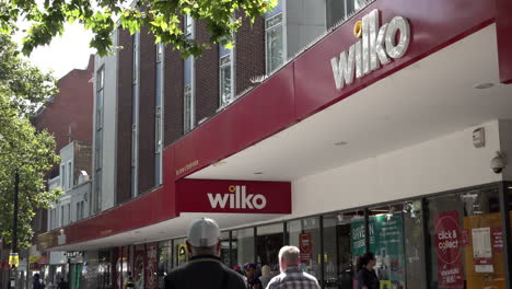 People-walk-past-the-storefront-of-a-Wilko-superstore-on-a-busy-high-street-in-Stratford-on-a-hot-summer-afternoon