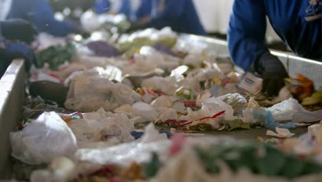 hands-of-workers-in-protective-suits-and-gloves-searching-through-piles-of-waste-lying-on-moving-conveyor-belt