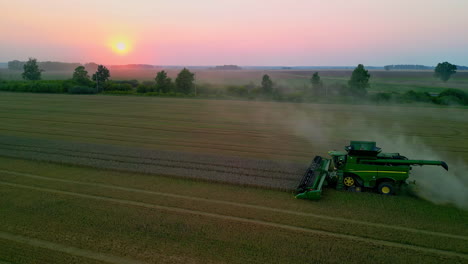Green-color-combine-harvester-working-from-early-hours,-aerial-view-during-sunrise