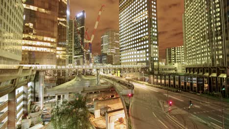 A-captivating-timelapse-unveils-an-intricate-cityscape-at-night,-teeming-with-tall-buildings-of-assorted-designs,-alongside-a-bustling-highway-arched-over-an-active-construction-site