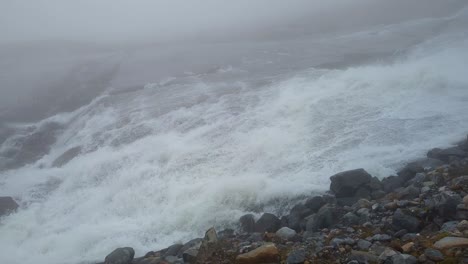 Pan-over-fast-flowing-glacier-river-in-remote,-stony-and-foggy-environment