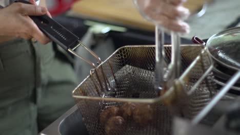 Deep-fried-meat-balls-freshly-pulled-out-of-hot-oil-vat-and-shaken-in-oil-strainer,-filmed-as-close-up-shot-in-handheld-slow-motion-style