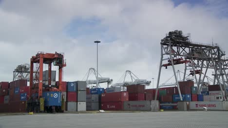 Detailed-depiction-of-a-crane-hoisting-containers-amidst-a-multicolored-container-stack-under-cloudy-skies,-in-a-concrete-shipping-yard