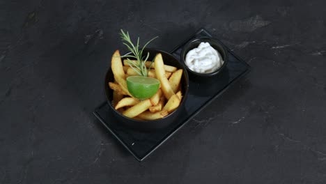 French-fries-garnished-with-rosemary-and-lime-next-to-a-mug-of-mayonnaise-are-presented-on-a-rotating-plate-